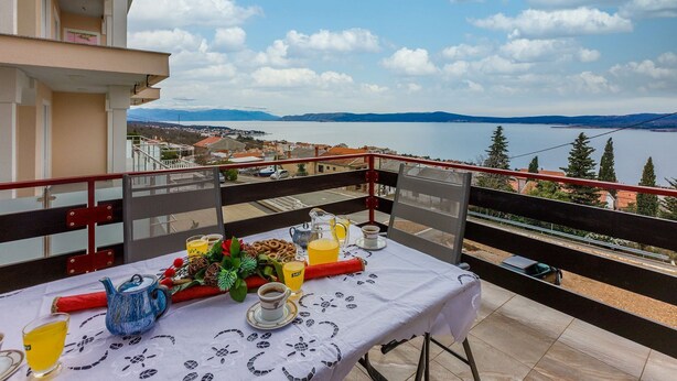 A balcony with a table set for breakfast, overlooking a lake and distant mountains. - Renovated flat with sea view, fitness room, baby cot, barbecue area (Crikvenica)