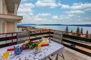 A balcony with a table set for breakfast, overlooking a lake and distant mountains.