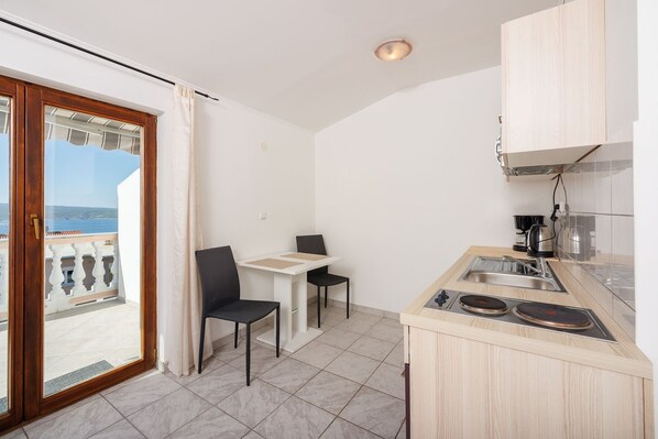 Une cuisine compacte avec un coin repas, une vue sur la mer et un balcon doté d’une balustrade en bois.