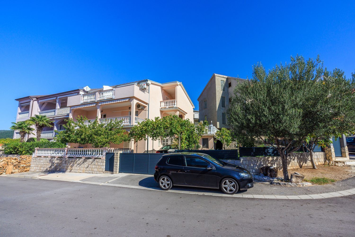 Um edifício residencial de vários andares com varandas, um carro estacionado e uma árvore em primeiro plano.
