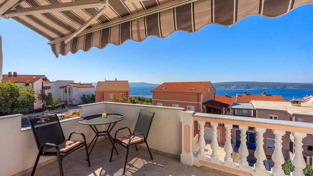 A balcony with a table and chairs, overlooking a coastal town with red-roofed buildings and a clear blue sky. - Idyllic studio flat with magnificent sea views, private car park, WiFi (Crikvenica)