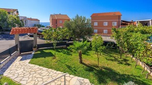 A residential area with a stone pathway leading to a gated entrance, surrounded by greenery and buildings with red-tiled roofs. - Idyllic studio flat with magnificent sea views, private car park, WiFi (Crikvenica)