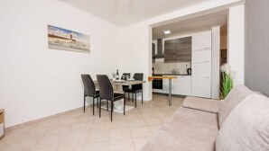 Une cuisine moderne avec des meubles blancs, un coin repas comprenant une table et des chaises, et un salon avec un canapé.