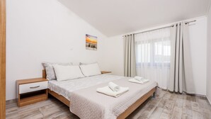 Une chambre à coucher avec un lit, une table de chevet, un tiroir en bois, un tableau au mur et une fenêtre avec des rideaux.