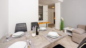 Un coin repas avec une table dressée pour quatre personnes, des chaises, un vase avec des fleurs et, au fond, une cuisine.
