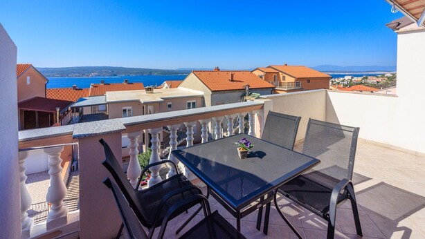 Un balcon avec une table et des chaises donnant sur une ville côtière.