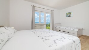 A bedroom with a large bed, a bedside table, a window with curtains, and a view of the outdoors. - Charming flat just 600 metres from the beach with sea views, charcoal grill, WiFi (Dramalj)