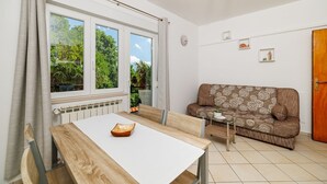 A modern living room with a wooden dining table, a brown sofa with a floral pattern, and a view of greenery through large windows. - Charming flat just 600 metres from the beach with sea views, charcoal grill, WiFi (Dramalj)