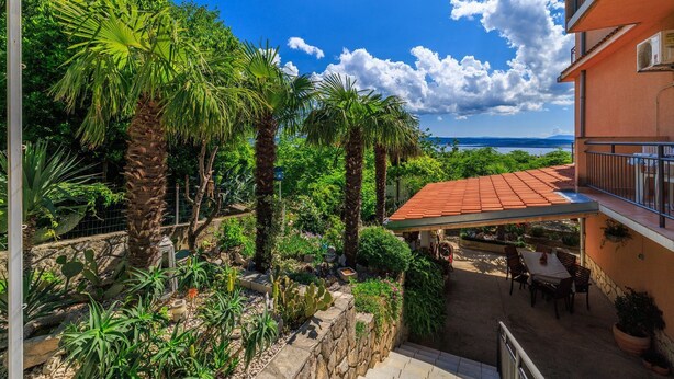 A courtyard with a covered patio, palm trees, and a view of the sea. - Charming flat just 600 metres from the beach with sea views, charcoal grill, WiFi (Dramalj)