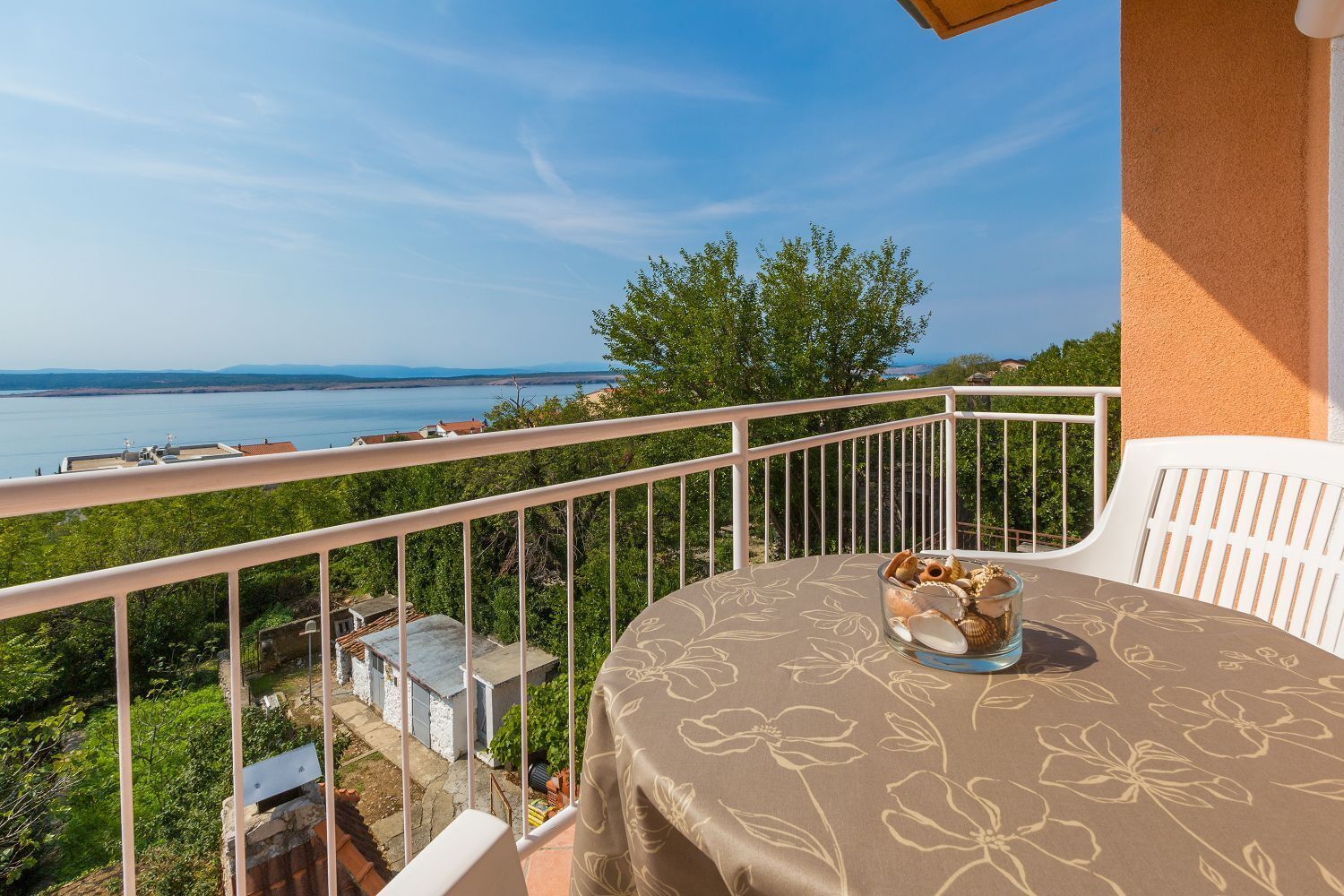 A balcony with a table and chairs, overlooking a body of water and greenery.