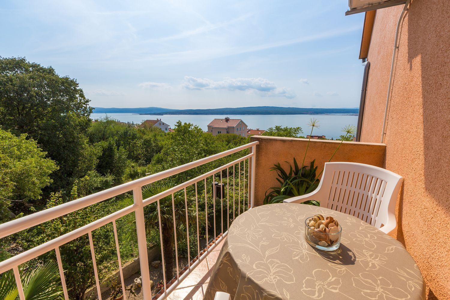 A balcony with a table and chairs, overlooking a scenic view of a lake and distant buildings.