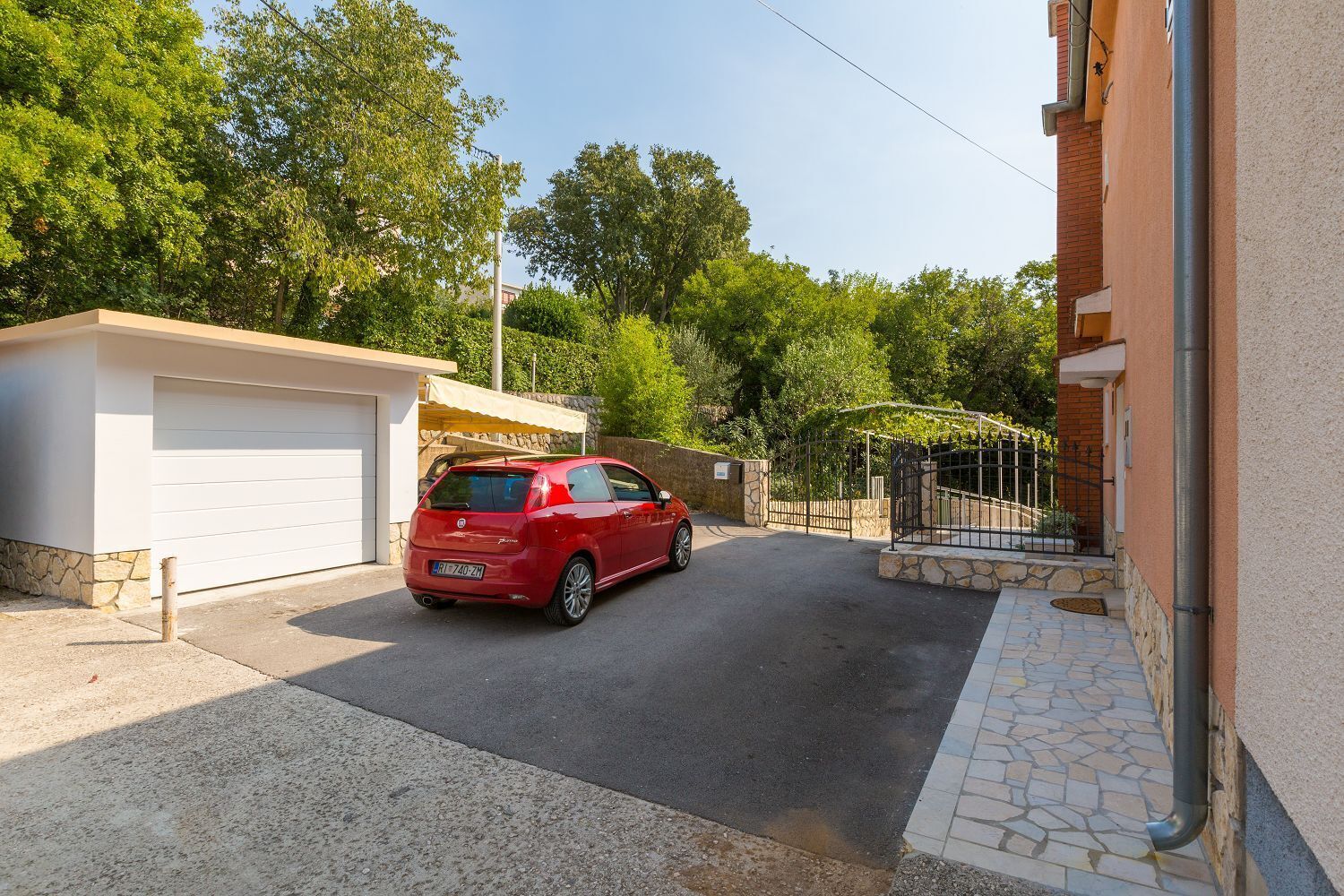 Un auto rojo estacionado en una entrada con un garaje y un muro de piedra.