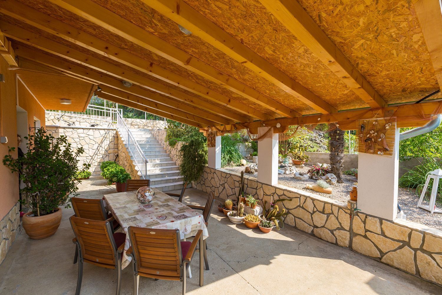An outdoor patio with a wooden pergola, stone walls, and a table with chairs.