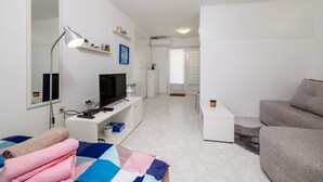 Ein modernes, helles Wohnzimmer mit Fernseher, weißen Möbeln und einer gemütlichen Sitzecke.