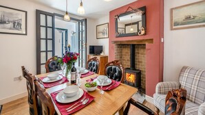 Un comedor con una mesa de madera dispuesta para cuatro, una chimenea y un televisor sobre un mueble de madera.