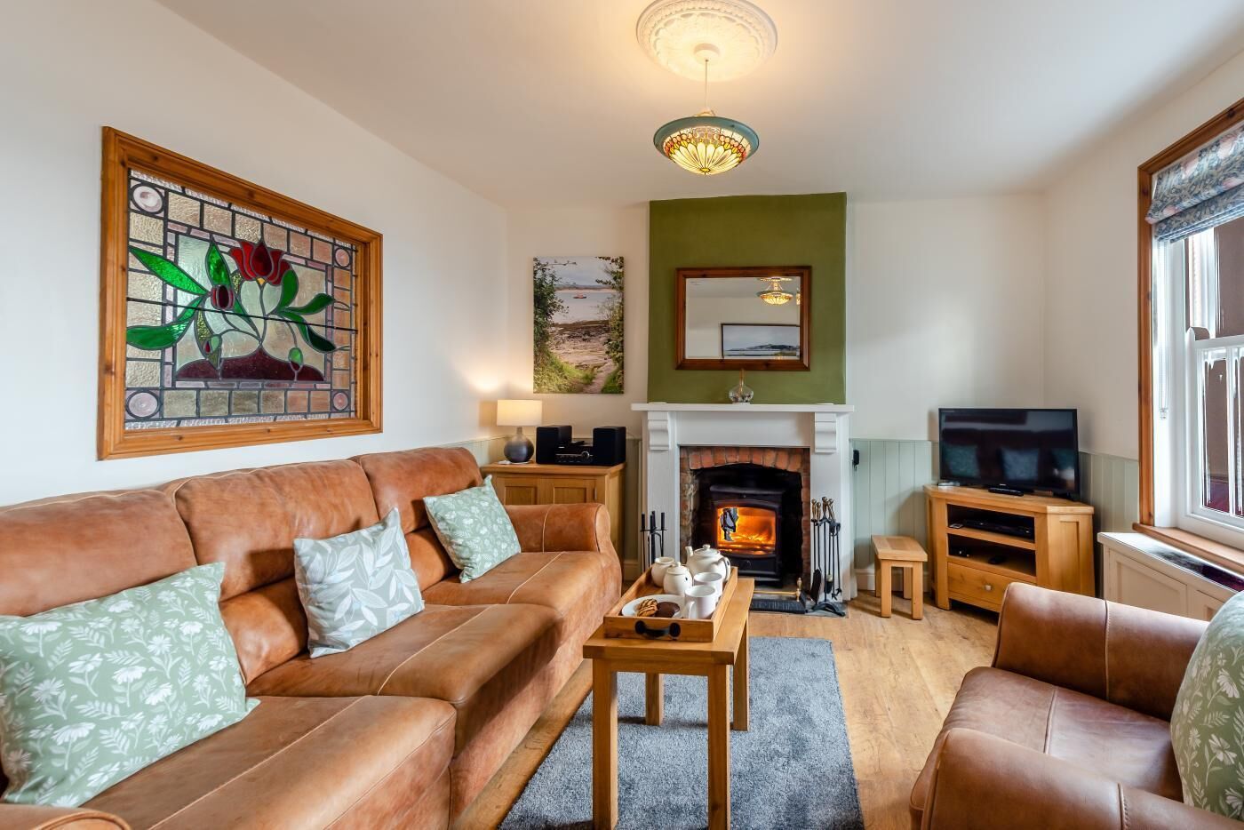 A living room with a sofa, a coffee table, a fireplace, a television, and a stained glass window.