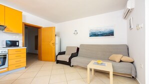 Un espace de vie compact comprenant un coin cuisine, un canapé, une petite table et une porte donnant sur une autre pièce.