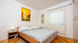 Une chambre à coucher avec un lit en bois, du linge de lit blanc, une table de chevet avec une lampe, une bibliothèque et deux tableaux accrochés au mur.