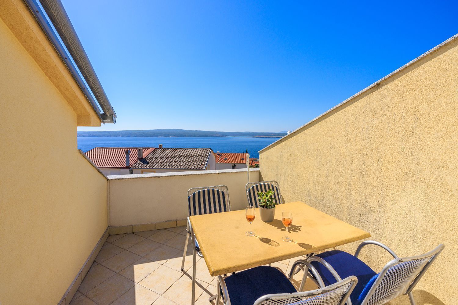 A small balcony with a table and chairs, overlooking a coastal view.