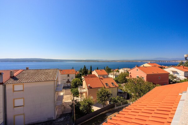 A coastal town with terracotta-roofed buildings, a clear blue sky, and a view of the sea.