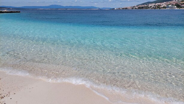 Una playa con agua turquesa cristalina, una orilla arenosa y una vista distante de un pueblo costero.