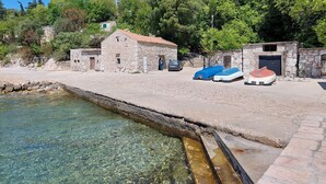 Un edificio de piedra con techo de tejas rojas, un pequeño muelle con barcos y agua cristalina.
