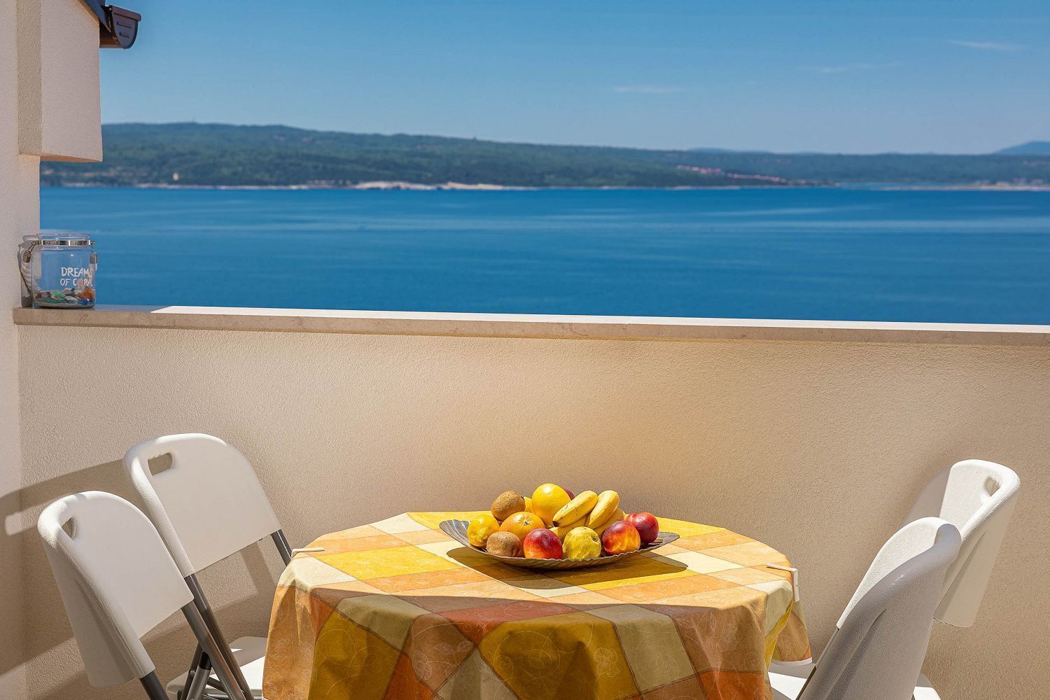 Een tafel met een fruitschaal op een balkon met uitzicht op water.