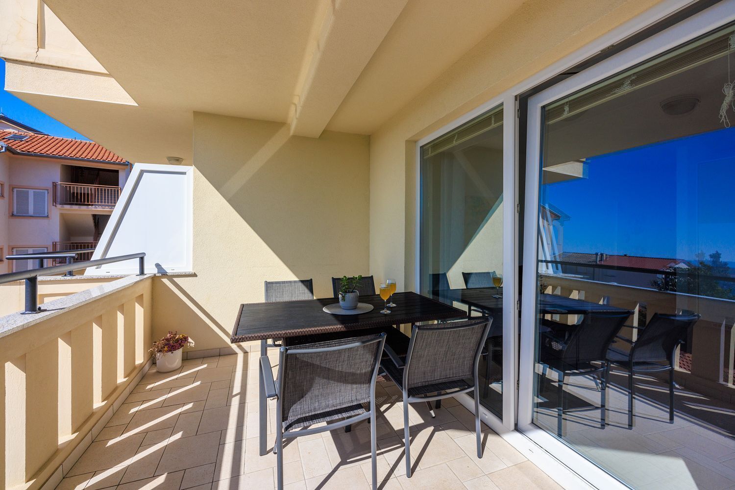 Een balkon met een tafel, stoelen, een bloempot en een glazen deur die uitkomt op een terras.