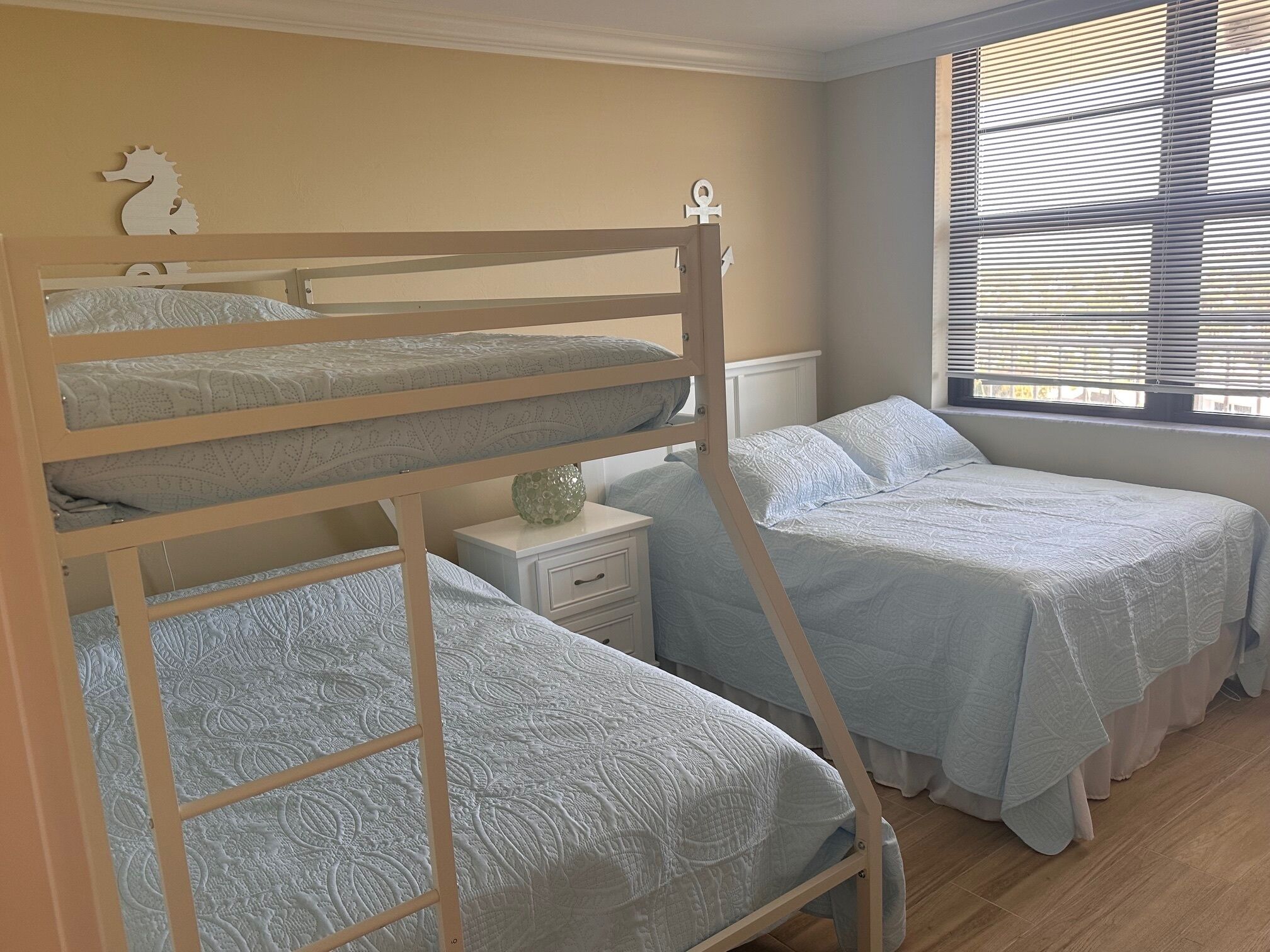 Quarto com beliche, janela e mesa de cabeceira.