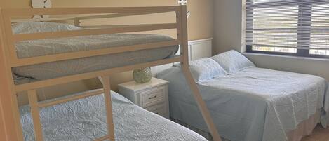 Quarto com beliche, janela e mesa de cabeceira.