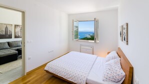 A bedroom with a bed, a window with a view, a sofa, and artwork on the walls. - Modern flat only 90 metres to the beach with sea view, underground car park, air conditioning (Crikvenica)