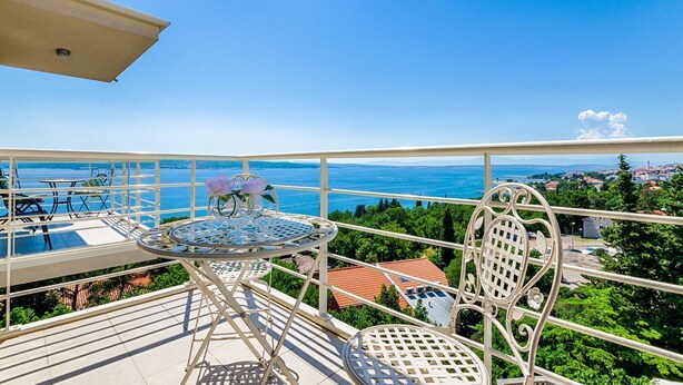 A balcony with a table and chairs, overlooking a scenic view of the sea and a coastal town. - Modern flat only 90 metres to the beach with sea view, underground car park, air conditioning (Crikvenica)