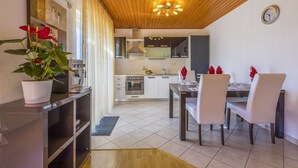 Une cuisine moderne avec des armoires blanches, un four encastré et une hotte de cuisinière en acier inoxydable. On y trouve un coin repas avec une table et des chaises, ainsi qu’une plante en pot posée sur le comptoir.