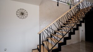Un escalier moderne avec des marches en bois et des rampes en métal noir, une horloge murale aux motifs géométriques et un mur sobre avec un revêtement texturé.