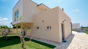 A modern two-story house with a flat roof, a stone pathway, and a small garden.