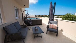 Une terrasse sur le toit aménagée avec un canapé, une chaise, une table, un fauteuil suspendu et un jacuzzi.