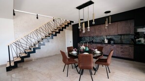 Une cuisine moderne avec des meubles de couleur sombre, un coin repas doté d’une table en marbre et un escalier au design géométrique.