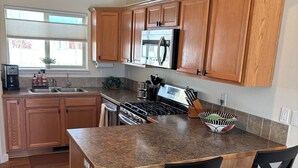 A kitchen with wooden cabinets, a stainless steel refrigerator, a built-in oven, and a granite countertop. There are two black chairs at the island.