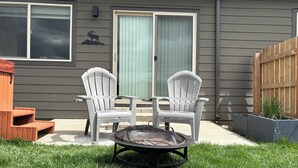 A patio with two Adirondack chairs, a round table, and a fire pit.