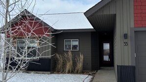 A residential building with a red and grey exterior, a covered driveway, and a snow-covered landscape.