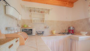 A compact kitchen with a microwave, a gas stove, and a sink. There are shelves above the sink holding cups and jars. - Charming studio flat with Mediterranean garden, barbecue, sun lounger, WiFi (Novigrad)