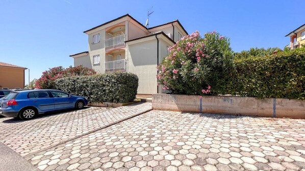 Un edificio residencial con entrada pavimentada, un automóvil estacionado y un arbusto grande con flores.