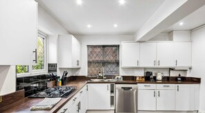 Una cocina moderna con armarios blancos, un refrigerador de acero inoxidable, lavavajillas y estufa negra.