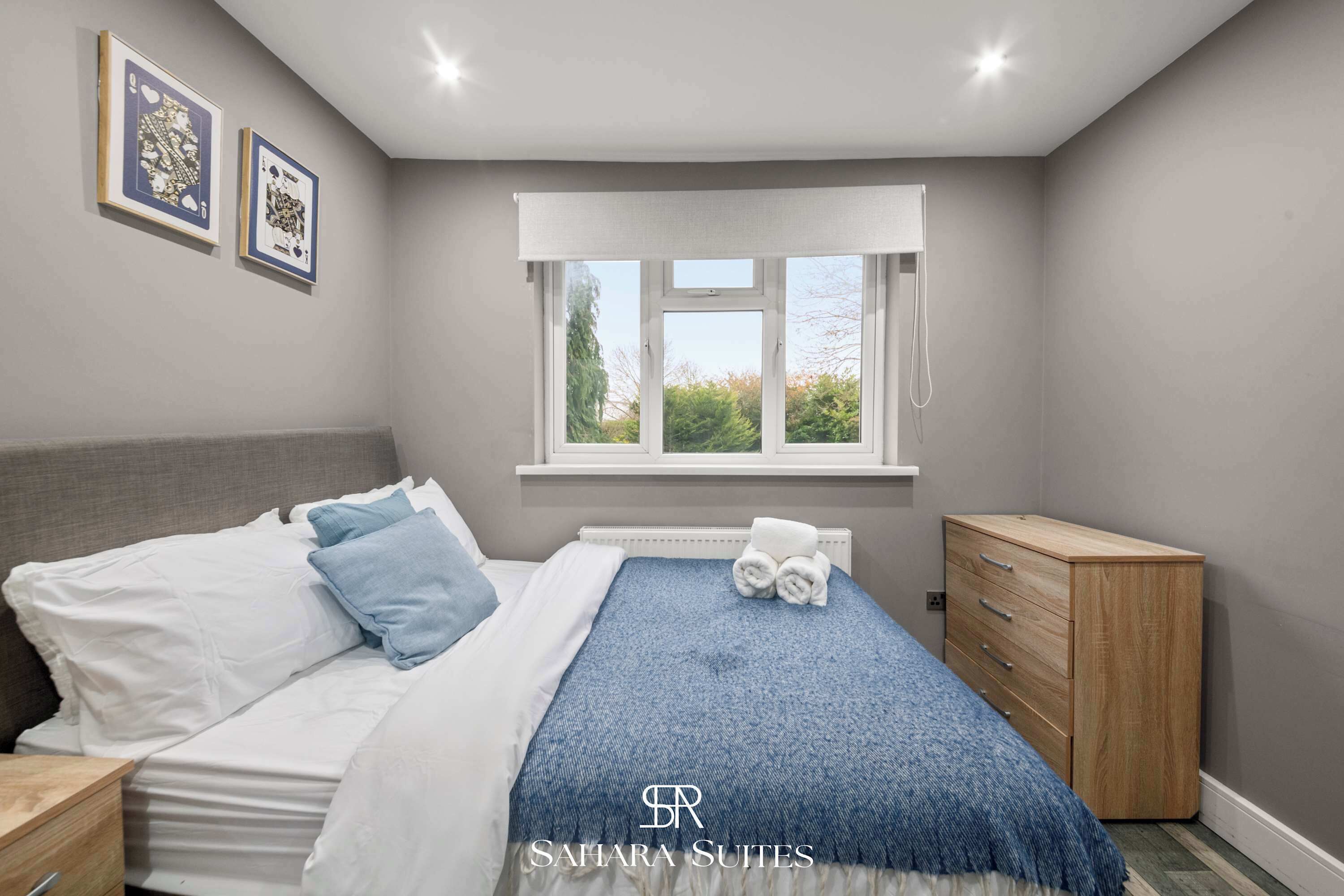 A bedroom with a bed, a dresser, a window, and framed pictures on the wall.