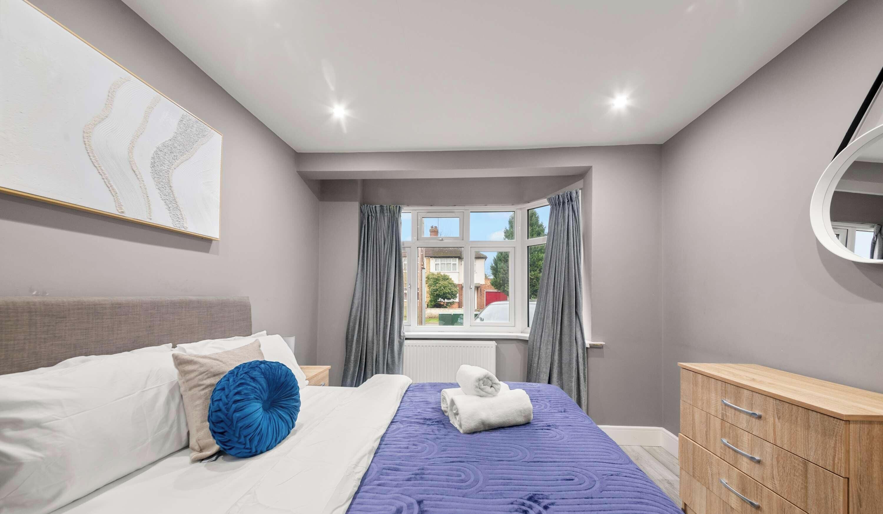 Une chambre à coucher avec un lit, une commode, une fenêtre avec des rideaux et un tableau accroché au mur.