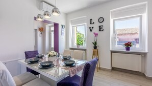 A modern dining area with a glass table, purple chairs, and a 'LOVE' wall decoration.