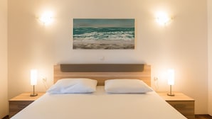 Una habitación de hotel con una cama grande, dos mesitas de noche con lámparas, y un cuadro del océano en la pared.
