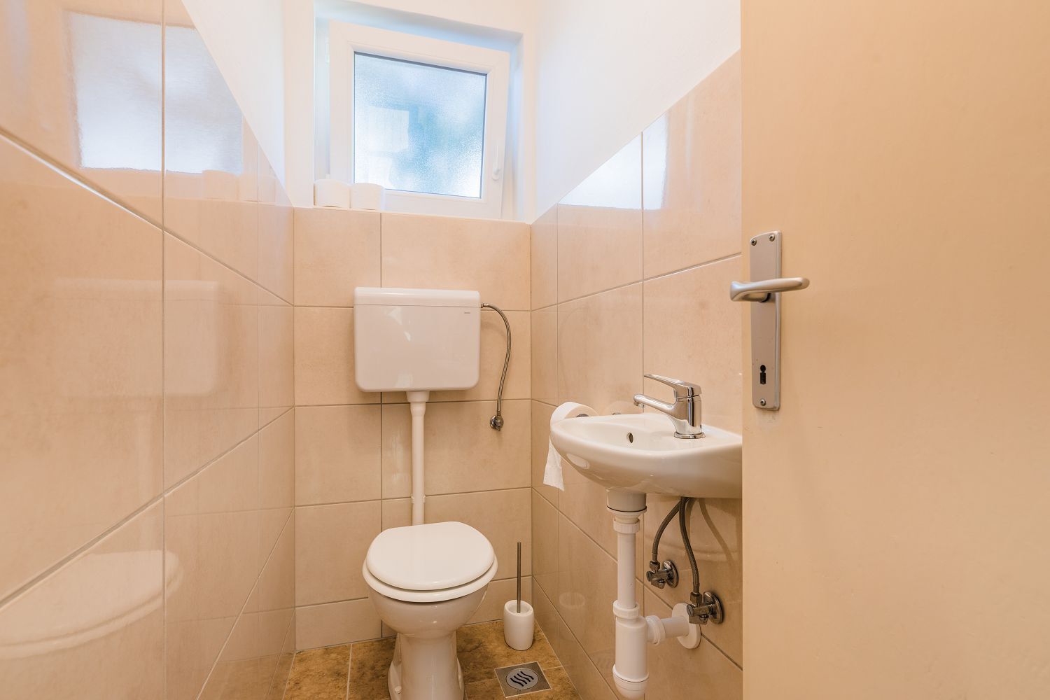 Une petite salle de bain avec des toilettes, un lavabo et une fenêtre.