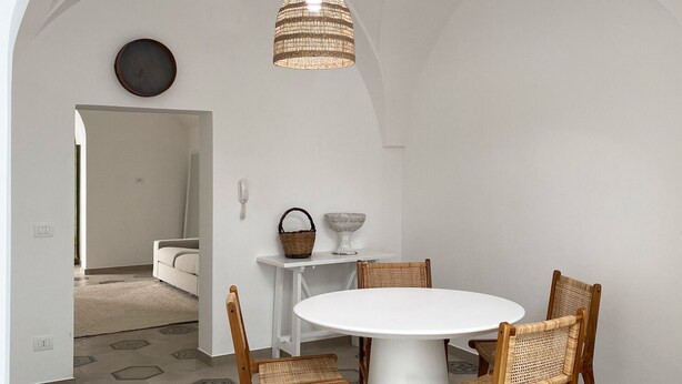 A dining area with a round table, four wicker chairs, a hanging light fixture, and hexagonal patterned floor tiles.
