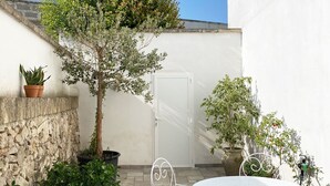 A patio with a white table and chairs, surrounded by potted plants and a stone wall.